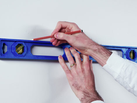 Hands using measuring tool and pencil against a white wall.