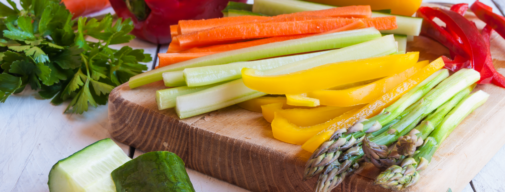 A wooden chopping board with sliced asparagus, capsicum, carrots, zucchini and more