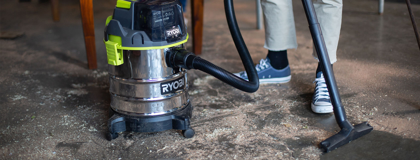 A man uses a RYOBI vacuum to clean sawdust off the workshop floor