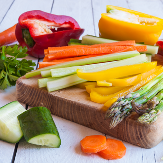 A wooden chopping board with sliced asparagus, capsicum, carrots, zucchini and more