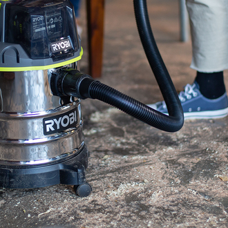 A man uses a RYOBI vacuum to clean sawdust off the workshop floor