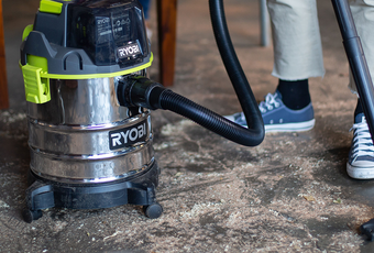 A man uses a RYOBI vacuum to clean sawdust off the workshop floor