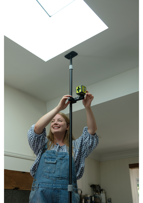 A closer shot of Brooke positions the RYOBI Green Cross Line Laser to find the centre of the wall