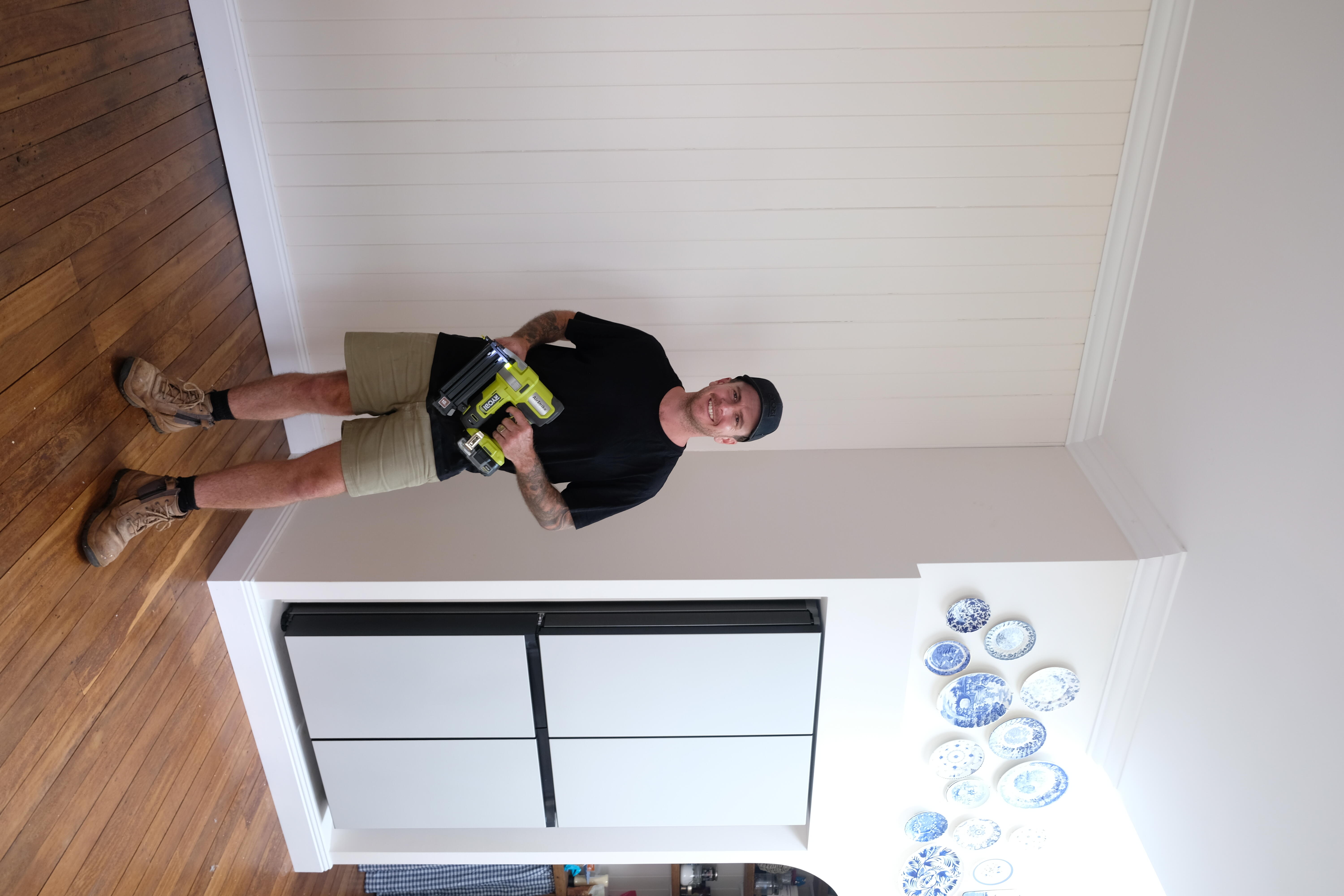 Jake stands proudly in front of freshly installed skirting boards. He’s holding a RYOBI brad nailer. 