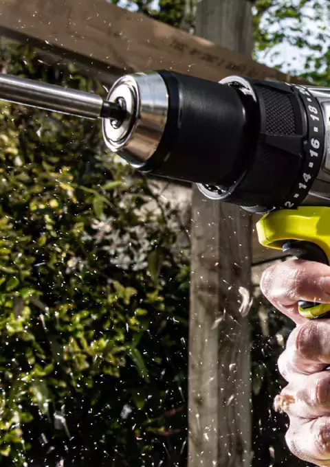 Lady wearing safety glasses drilling into upright wooden plank