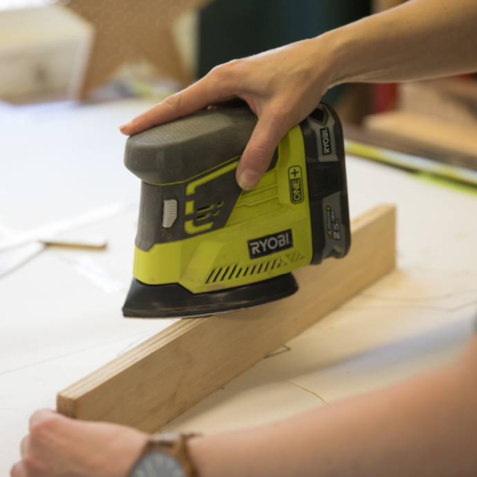 A Ryobi palm sander used to sand down a plank of wood