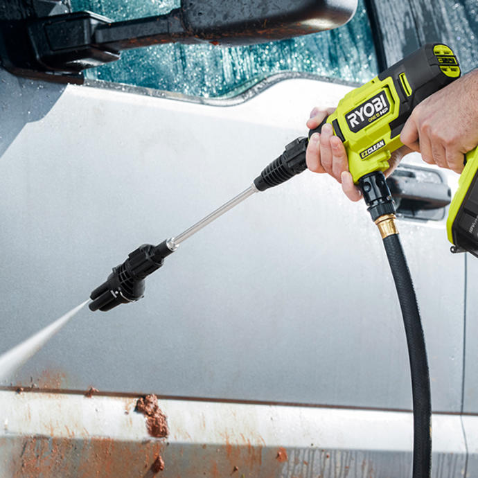 Using a Ryobi pressure washer to blast mud off a grey car