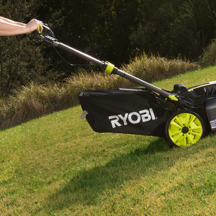 A man wearing a white shirt and tan pants pushes a Ryobi lawn mower